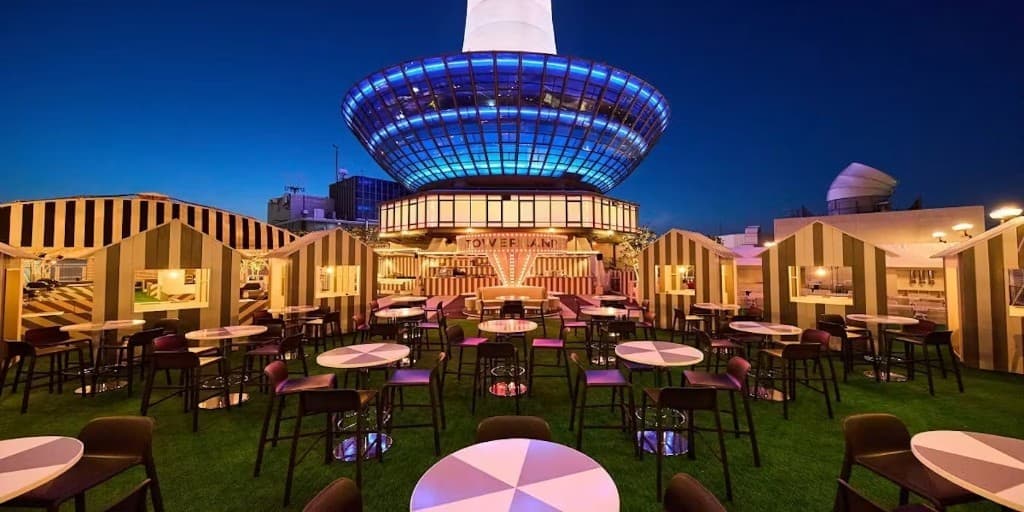 Towerland terrace under Kyoto Tower — green turf, striped cabanas, and the lit tower base